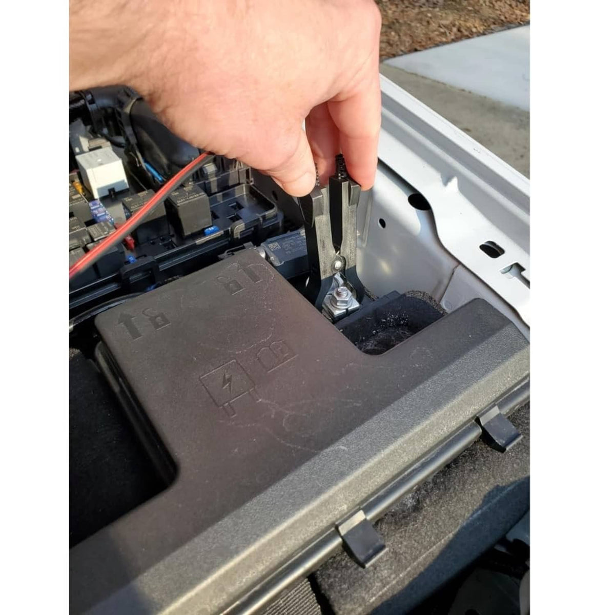 Hand using the relay tester to plug into a car fuse box socket area