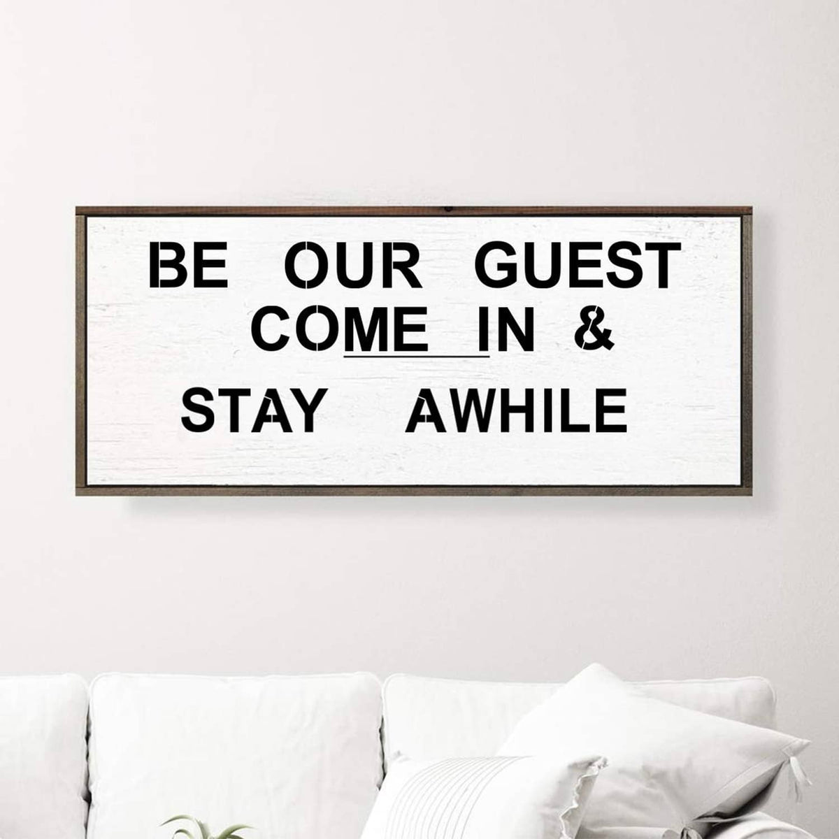 Framed sign made with letter stencils reading “BE OUR GUEST COME IN & STAY AWHILE”