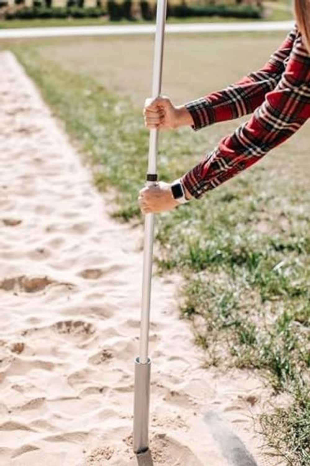 Ground flagpole mount staked into sand with pole held by hands