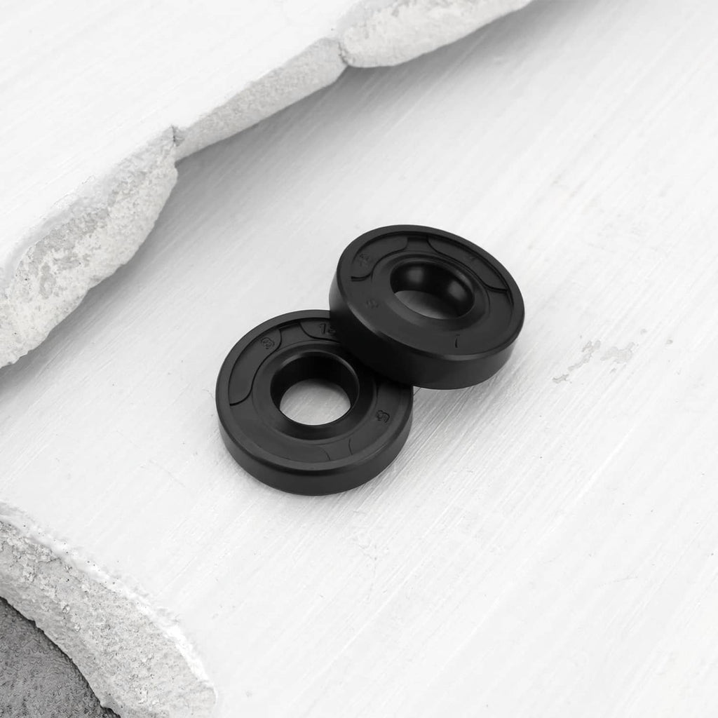 Two black shaft seals resting on white stone, molded seal profile