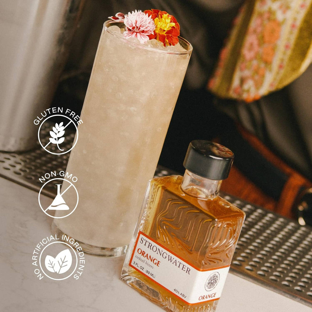 Orange bitters bottle beside a tall iced cocktail with flower garnish