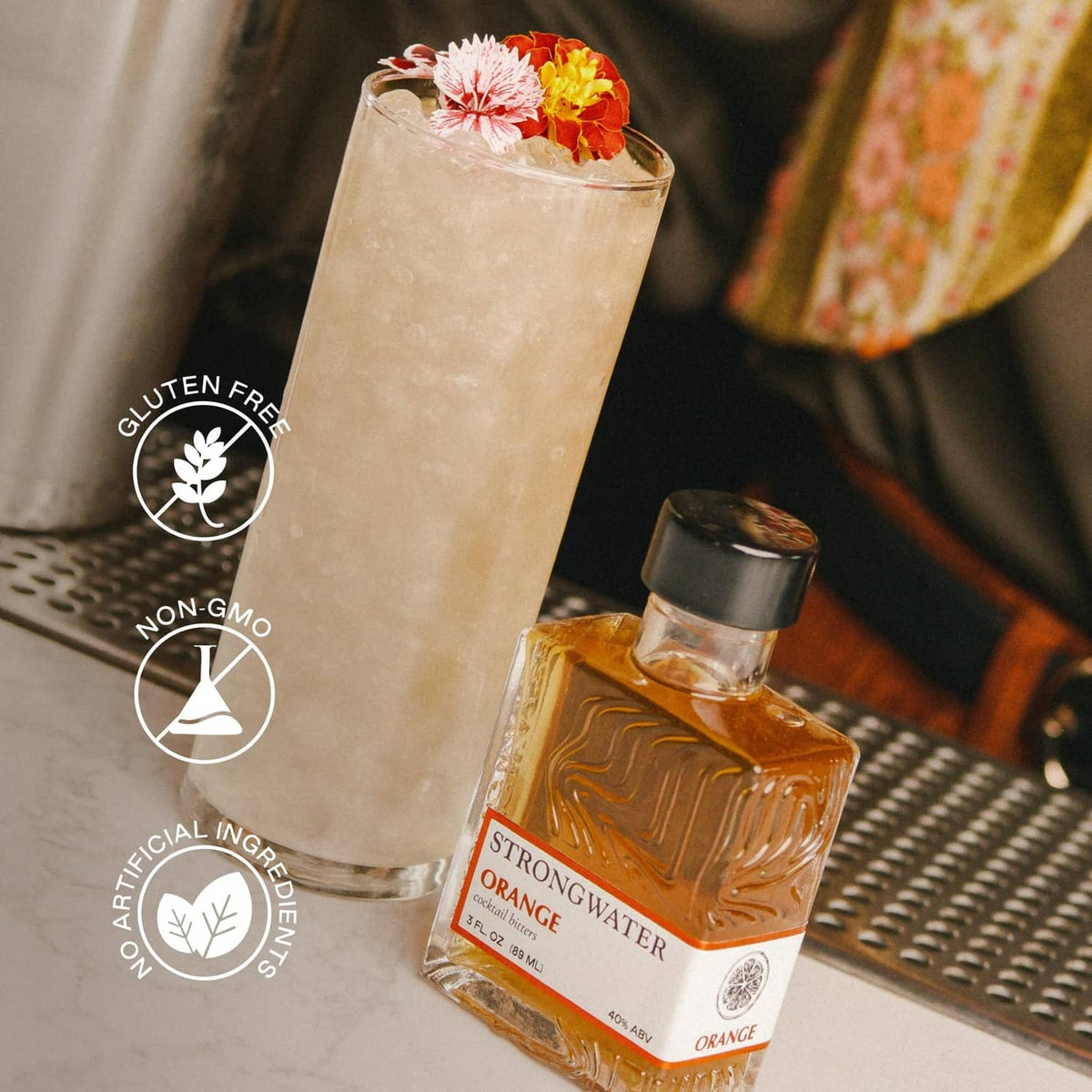 Orange bitters bottle beside a tall iced cocktail with flower garnish