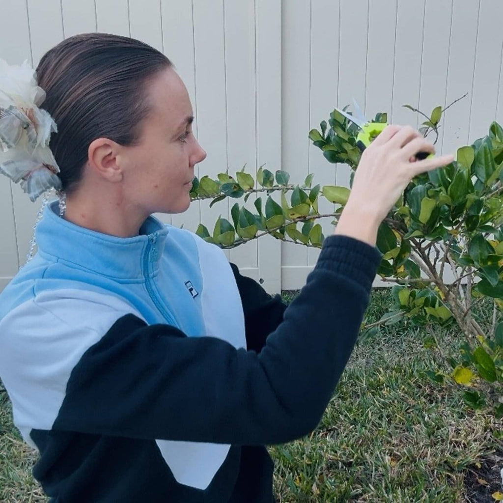 Green pruning shears held by a person trimming plants near a fence