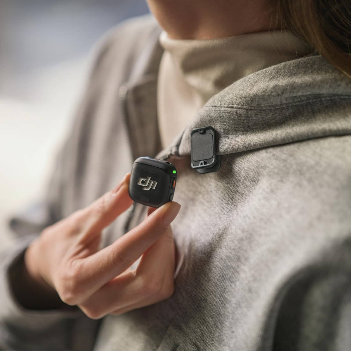 Black wireless mini microphone transmitter clipped to a gray jacket lapel.