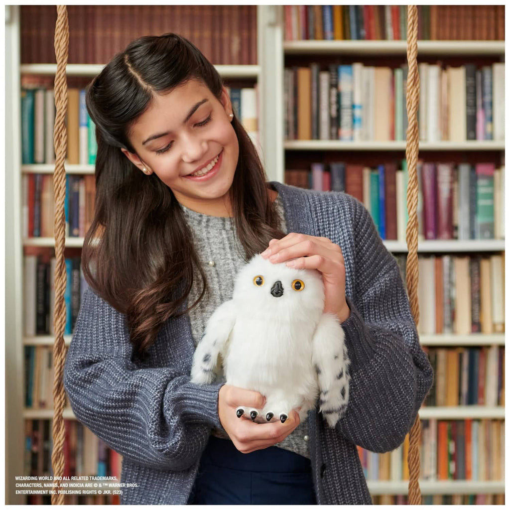 Person holding a white owl plush, showing amber eyes and spotted wings on its stand.