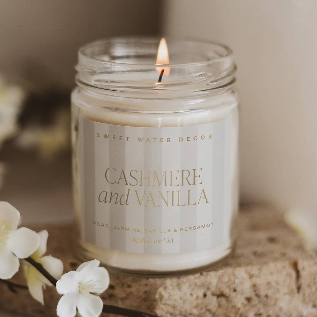 Lit cashmere and vanilla candle in glass jar with white blossoms near the jar