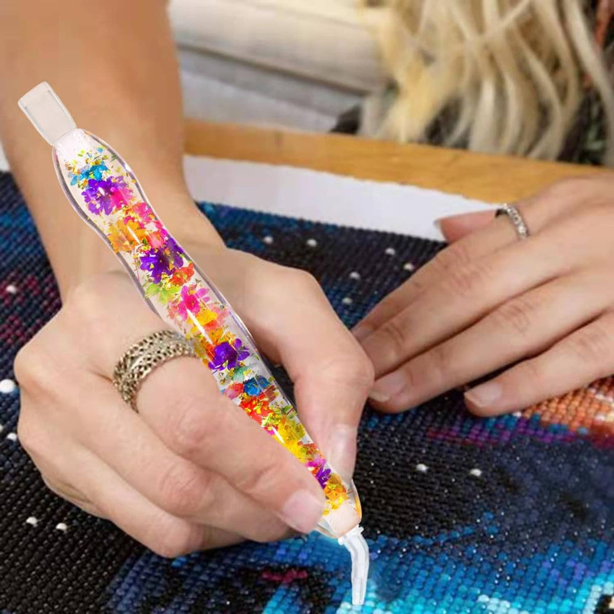 Diamond painting gem picker pen with multicolor glitter, held by hands over blue canvas