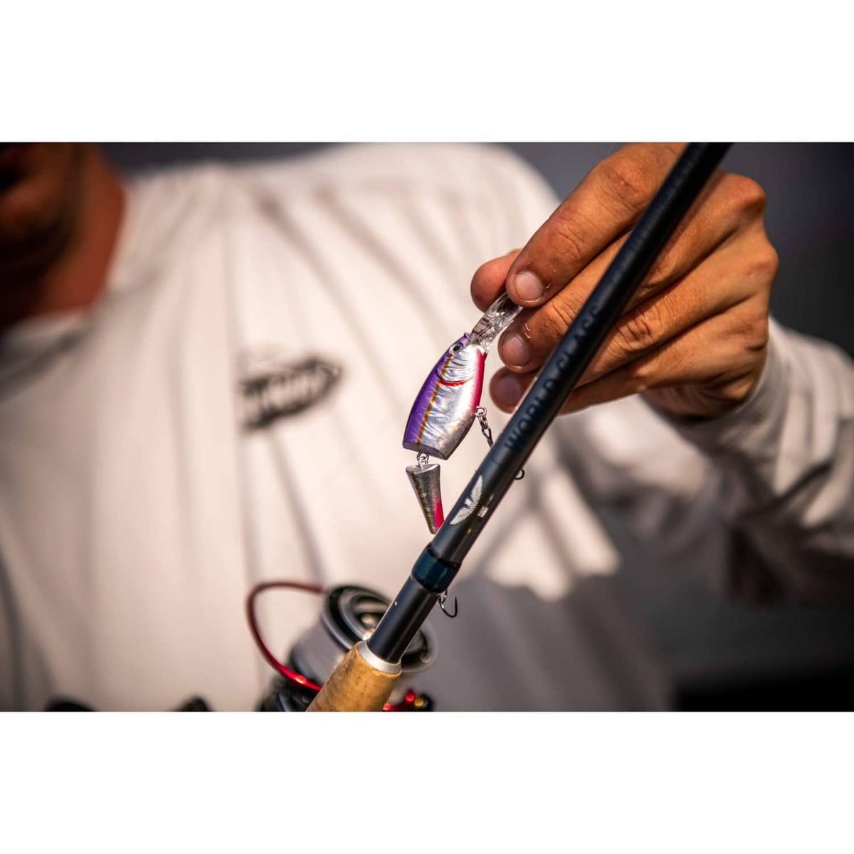 Purple and silver crankbait lure with treble hooks, held by a fisherman's hand