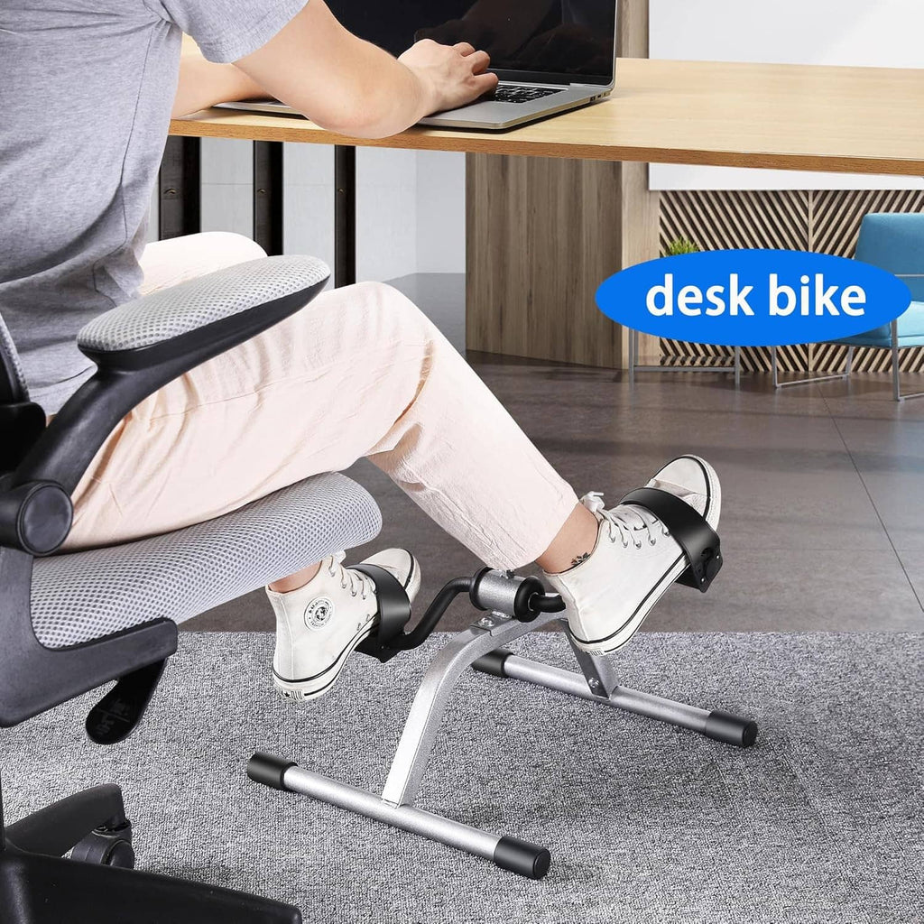 Mini exercise pedal bike used under a desk with feet on pedals and hands on handlebar