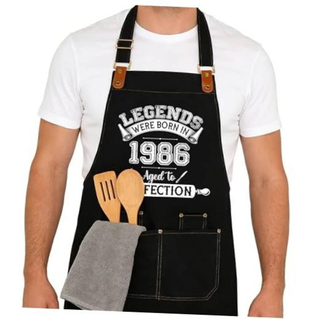 Black apron with printed 1986 design, adjustable straps, and front utility pockets.