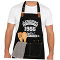 Black apron with printed 1986 design, adjustable straps, and front utility pockets.