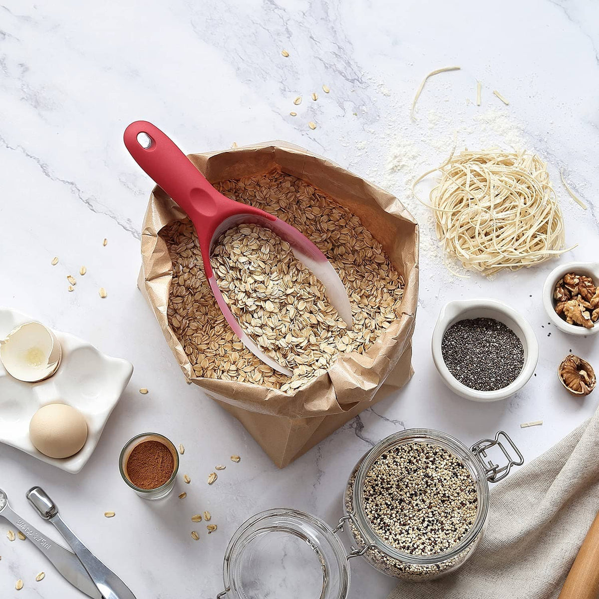 Red ice scoop resting in a pile of oats and seeds with small jars nearby