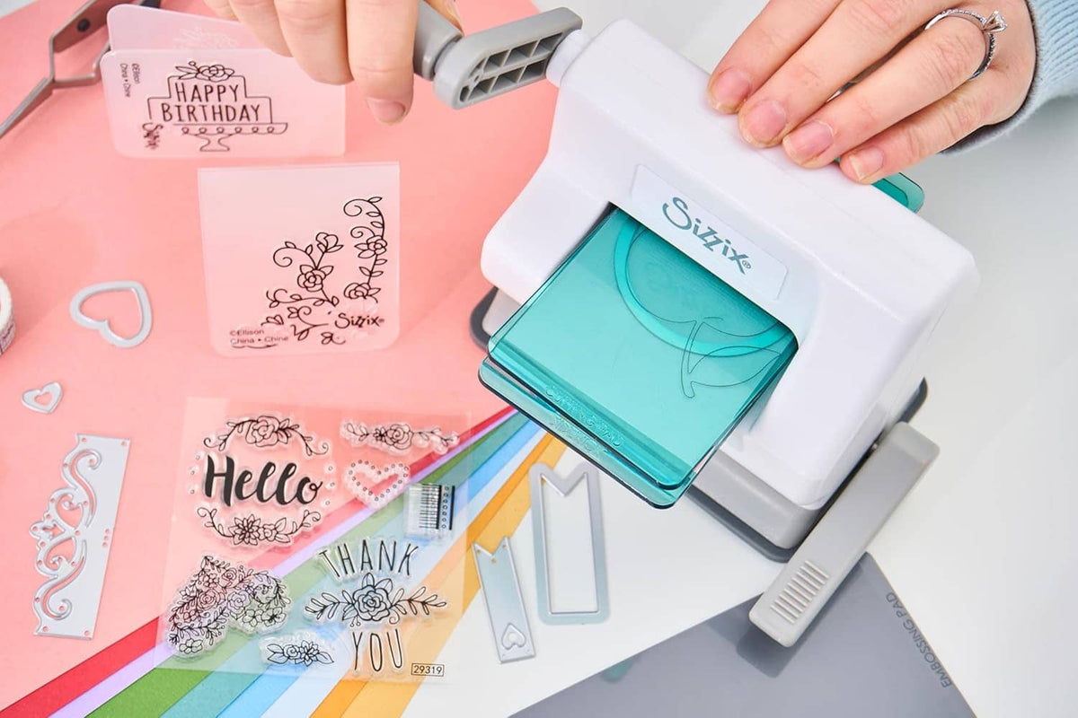Hands using white manual die-cutting machine with teal plate and greeting cards