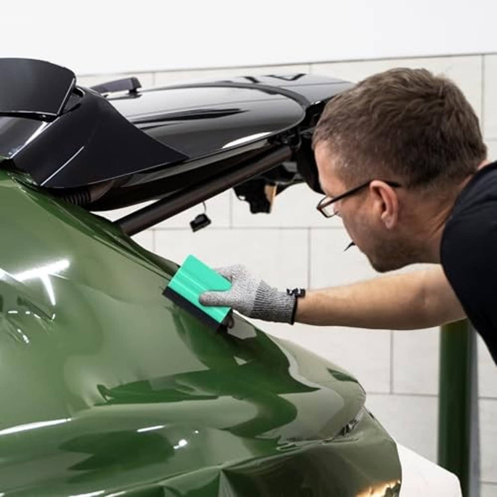 Hand using teal felt squeegee tool to smooth a glossy vinyl car wrap