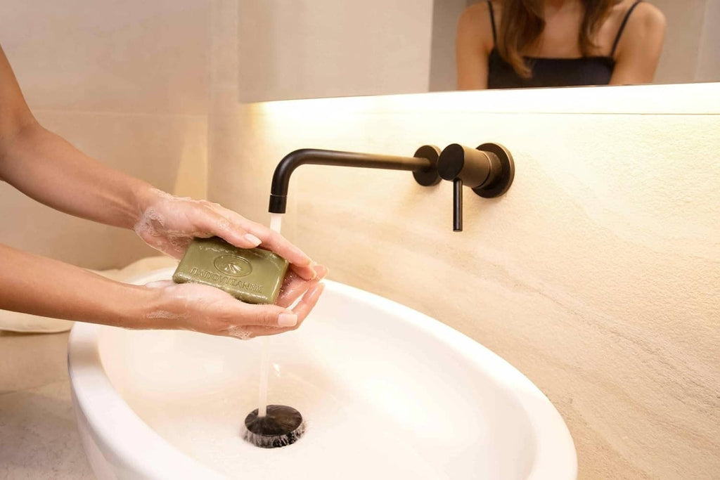 Olive oil bar soap held in hands above a white sink
