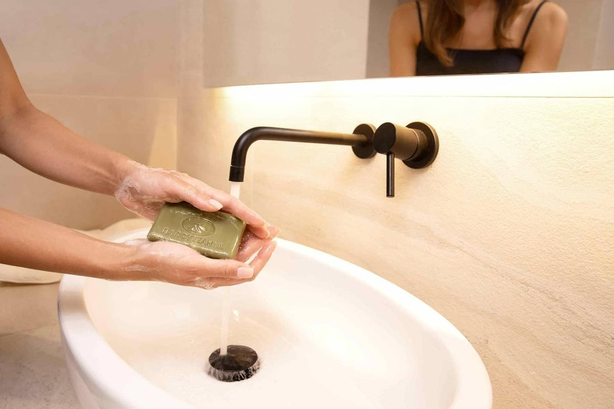 Olive oil bar soap held in hands above a white sink