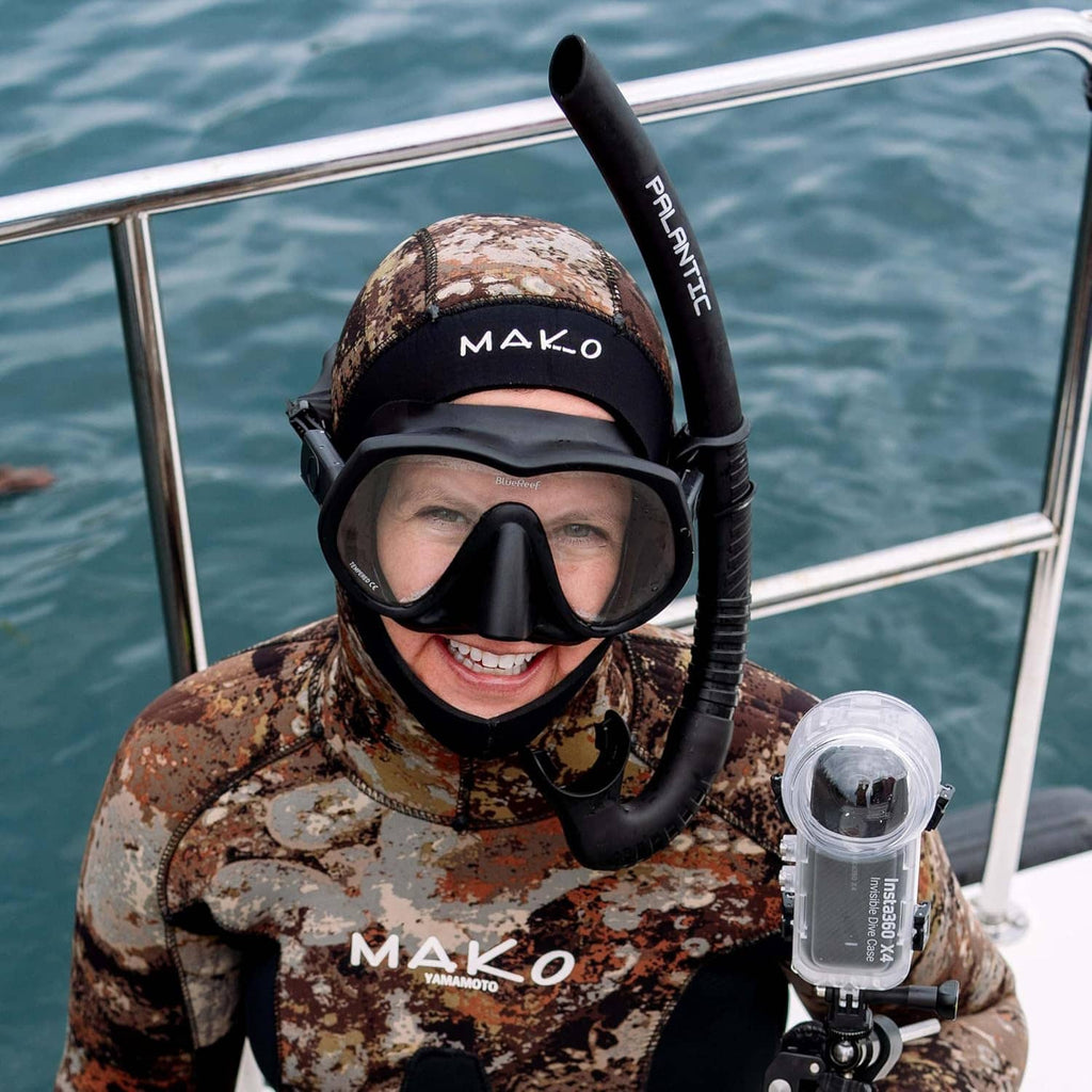 Anti-fog lens cleaner bottle held near scuba mask and goggles