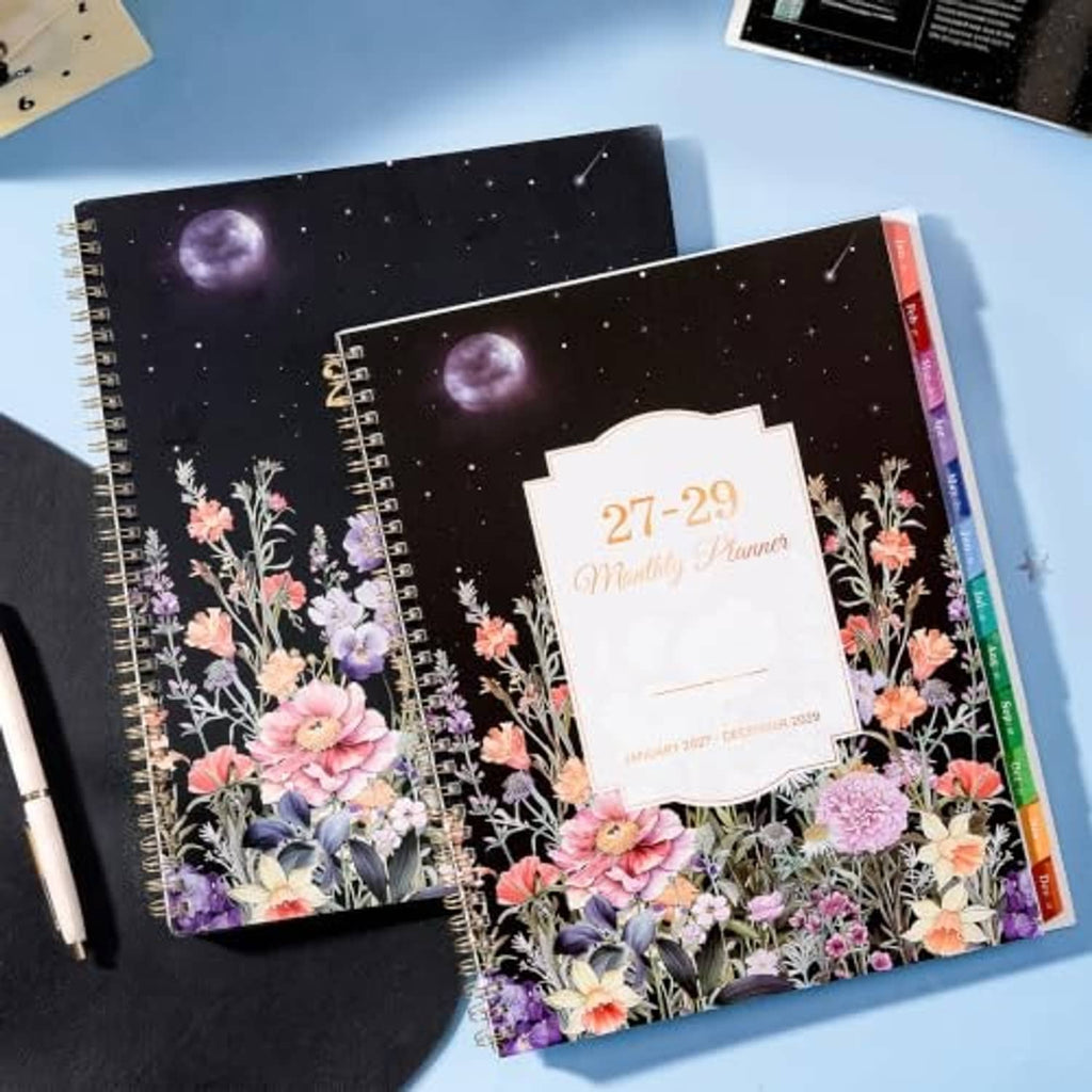 Two 2027-2029 floral monthly planners with black starry covers and gold spiral binding