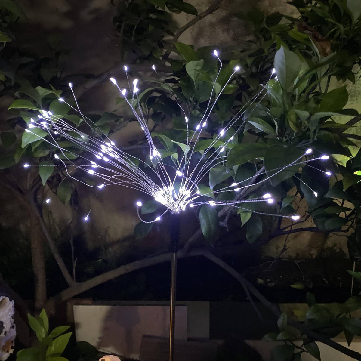 Solar firework stake light with cool-white LED burst among dark green leaves