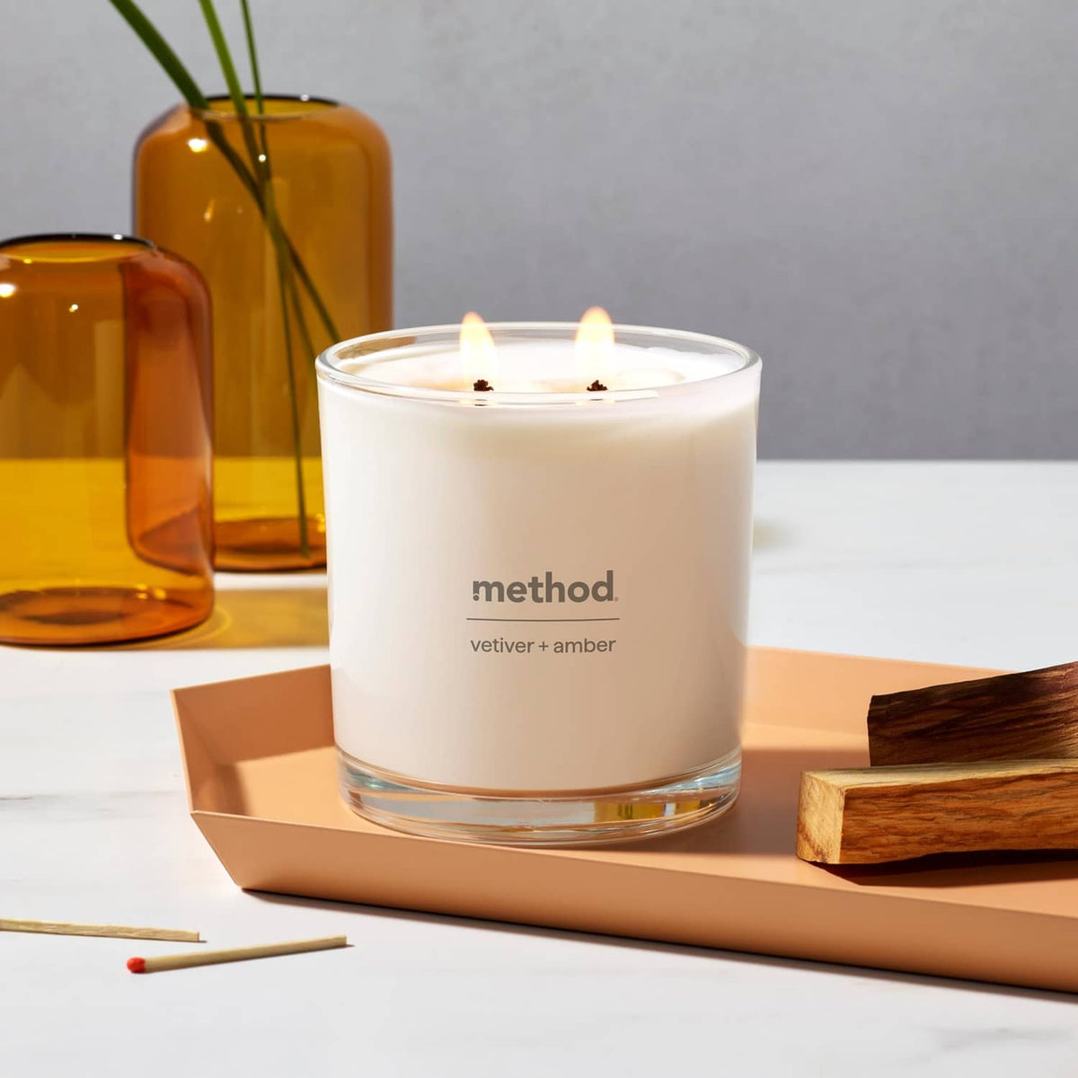 Two-wick soy candle in clear glass jar with white wax on wooden tray and matches