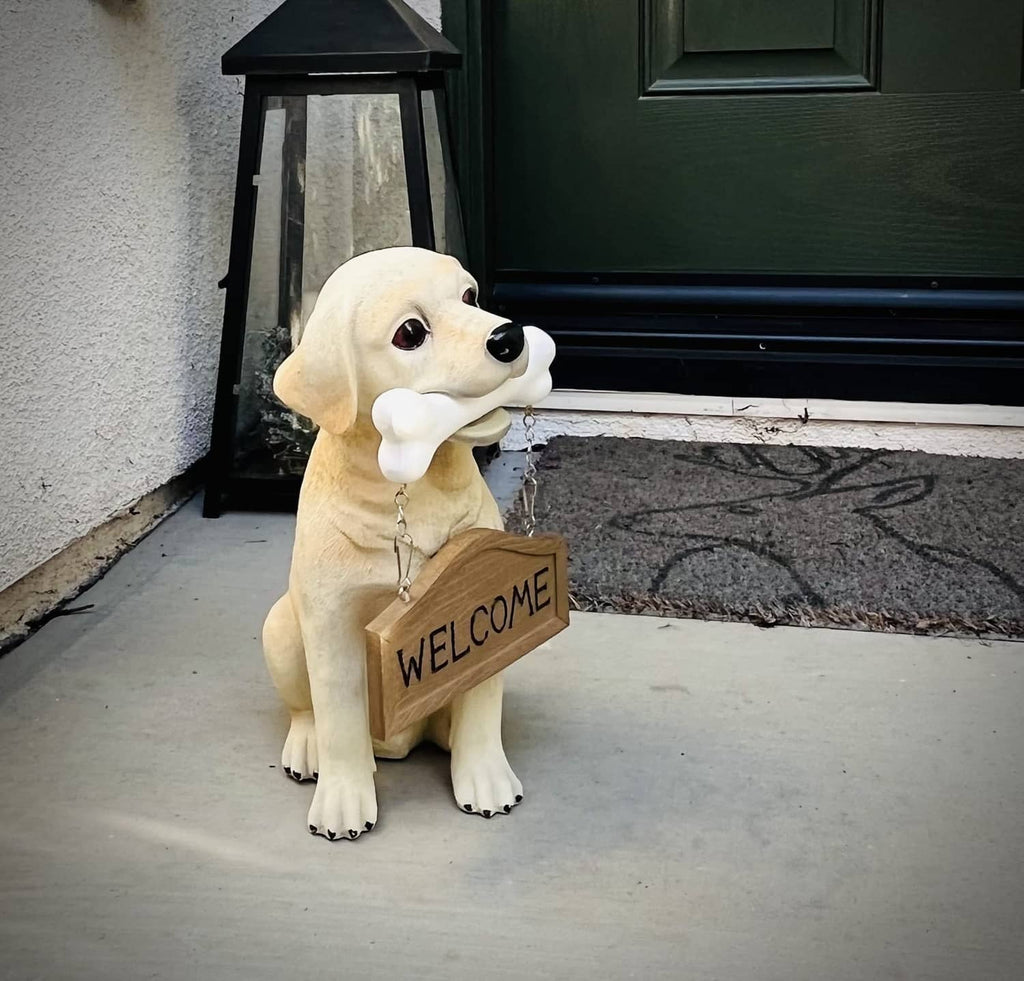 Tan Labrador puppy statue sitting with a white bone and a “WELCOME” wooden sign