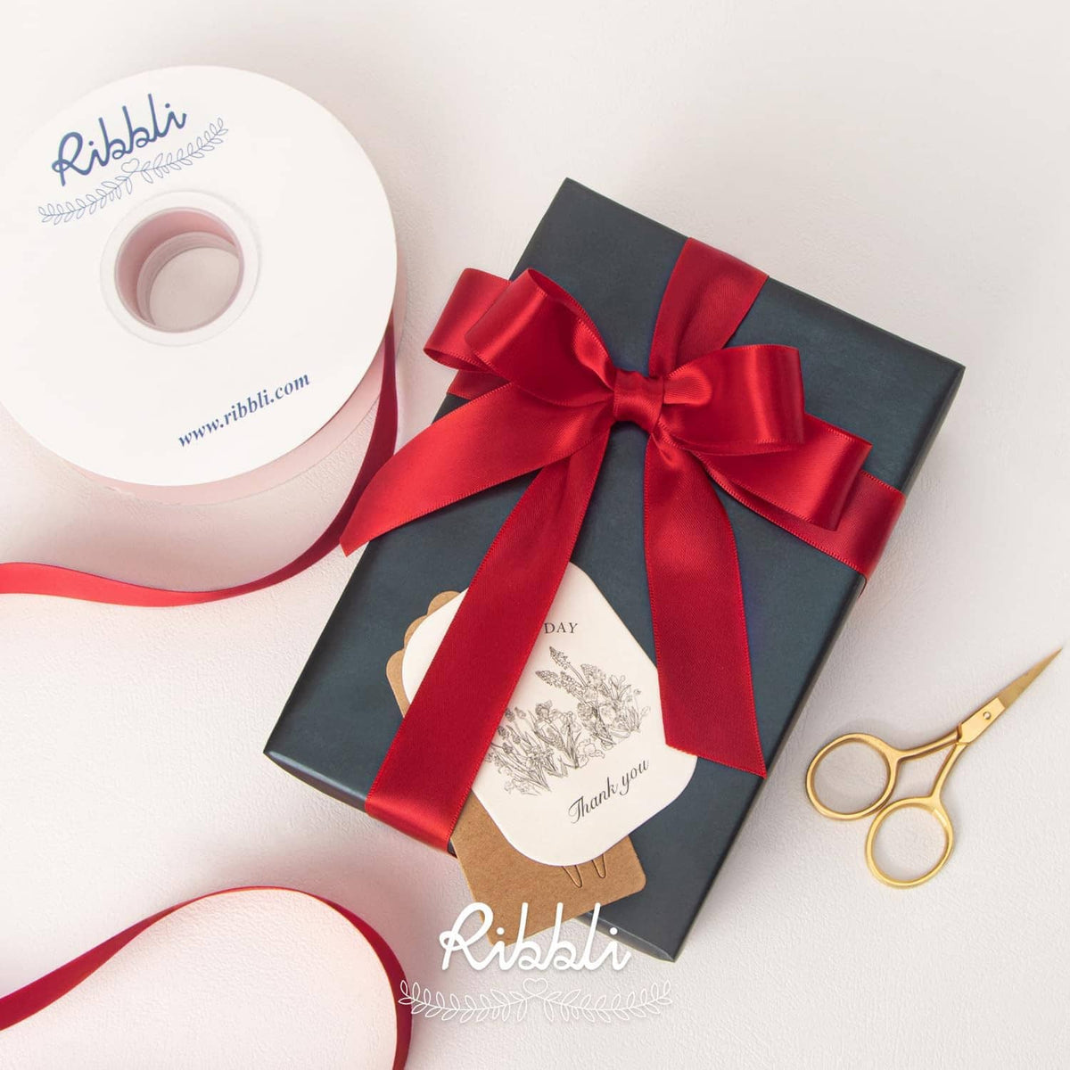 Red double-faced satin ribbon and roll beside a gift box with a bow