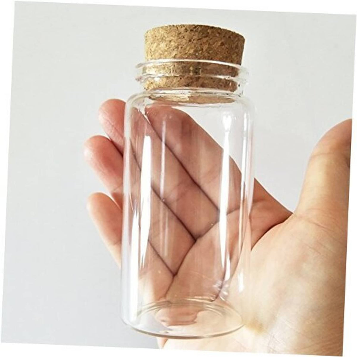 Small clear glass bottle vial with cork stopper, hand holding, front view, cylindrical glass