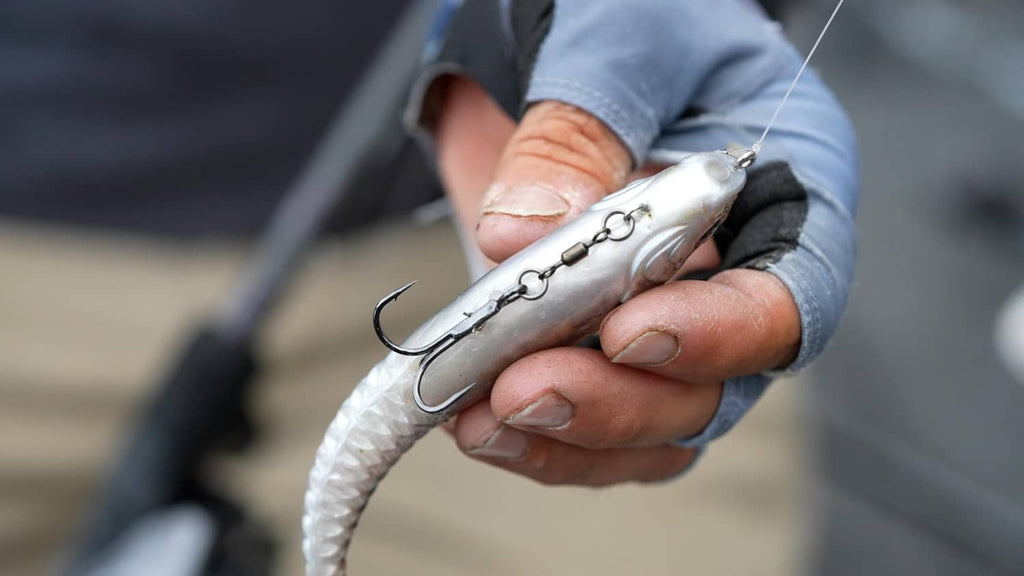 Silver soft plastic swim bait lure with exposed hook, held in hand