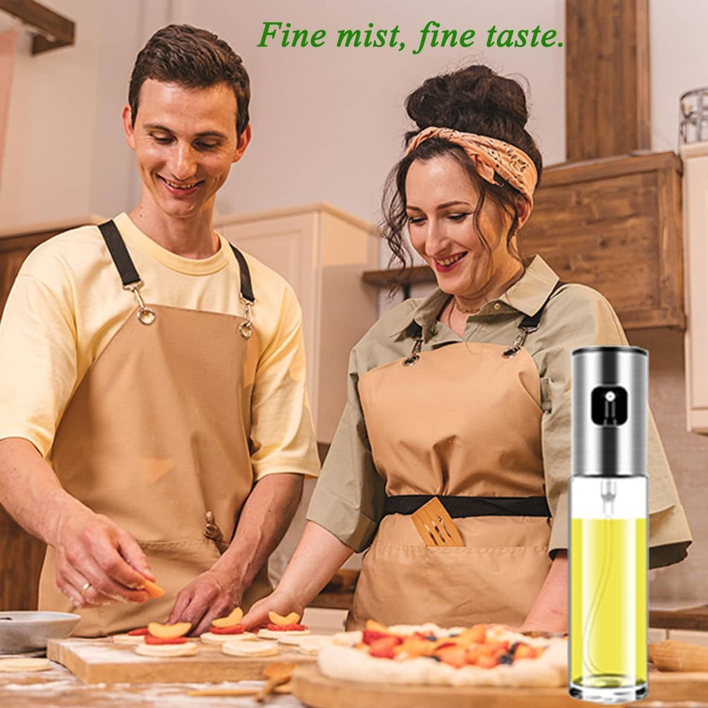 Stainless steel oil sprayer bottle with clear reservoir and yellow liquid in kitchen hands