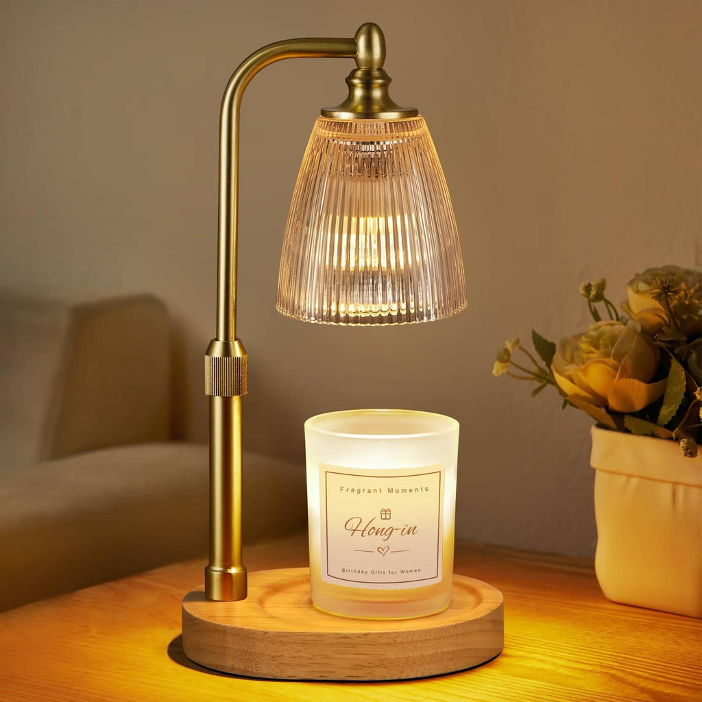 Clear bell-shaped candle warmer with brass stand and lit jar candle on wooden base