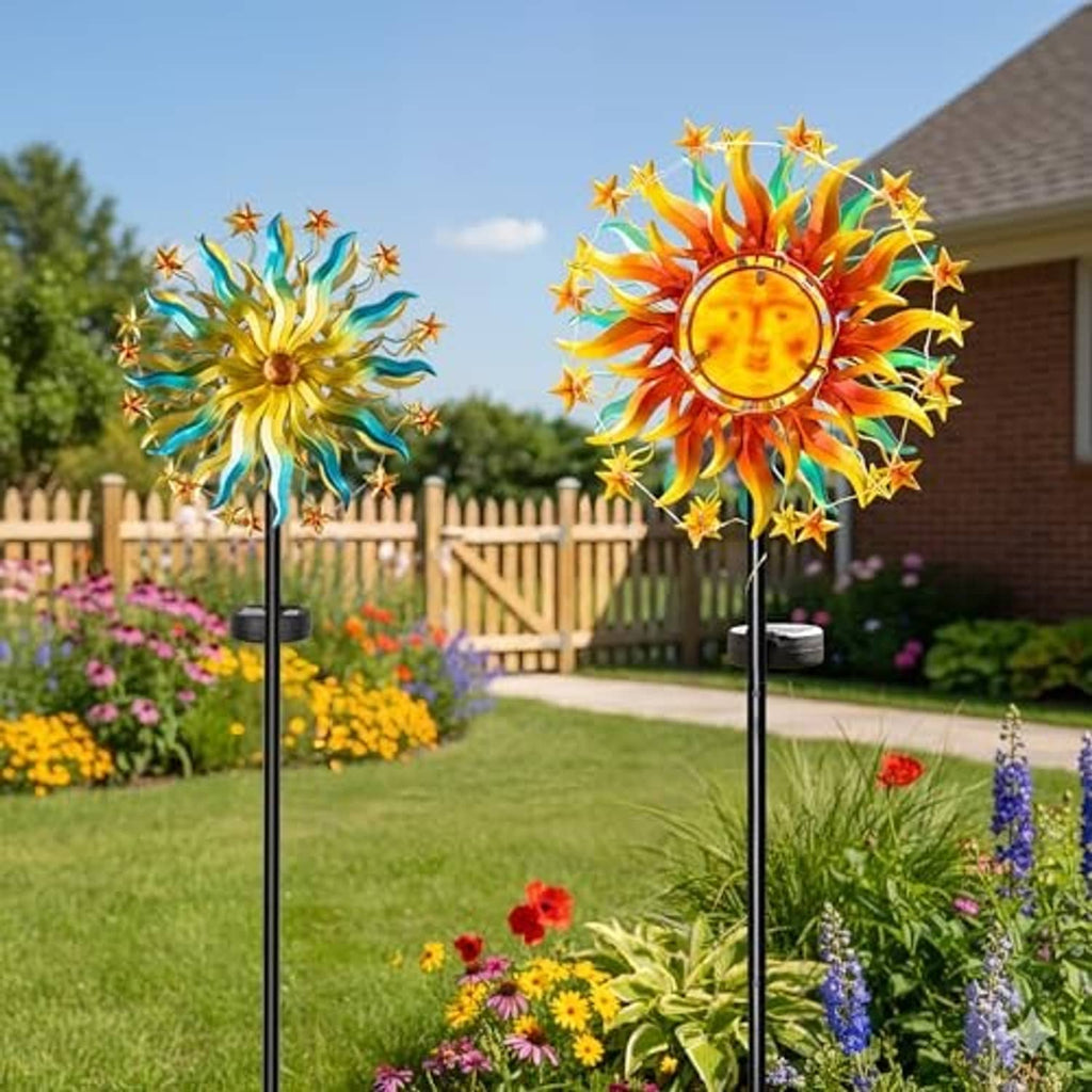 Two solar sun wind spinners with colorful rays displayed among flowers and grass.