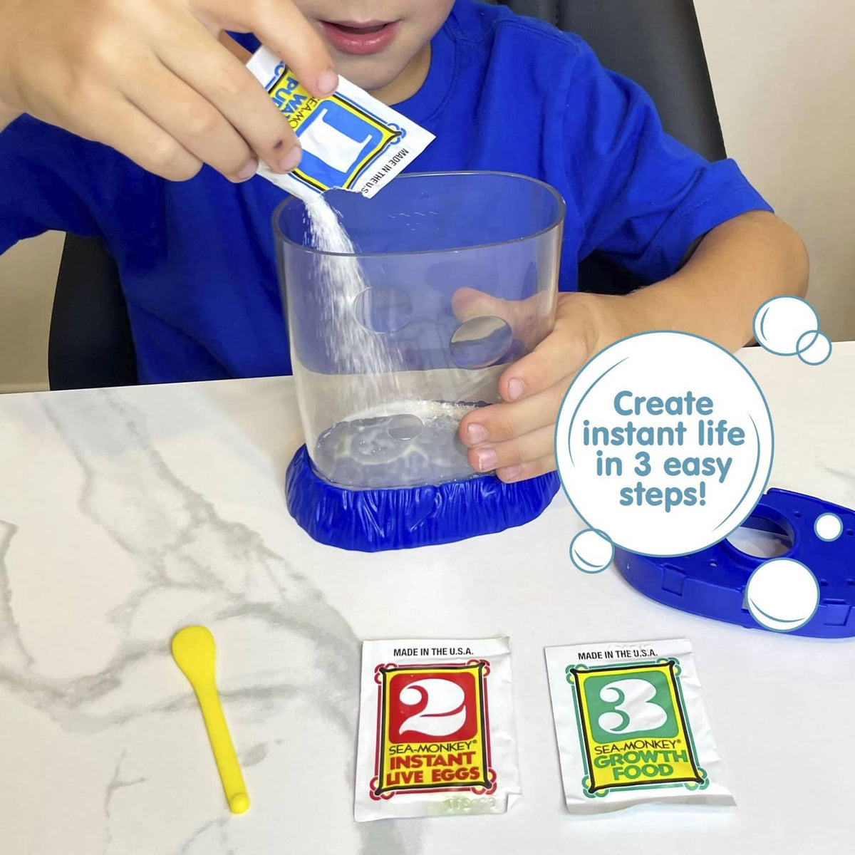 Magiquarium starter kit in use: child pours water into clear tank with blue base