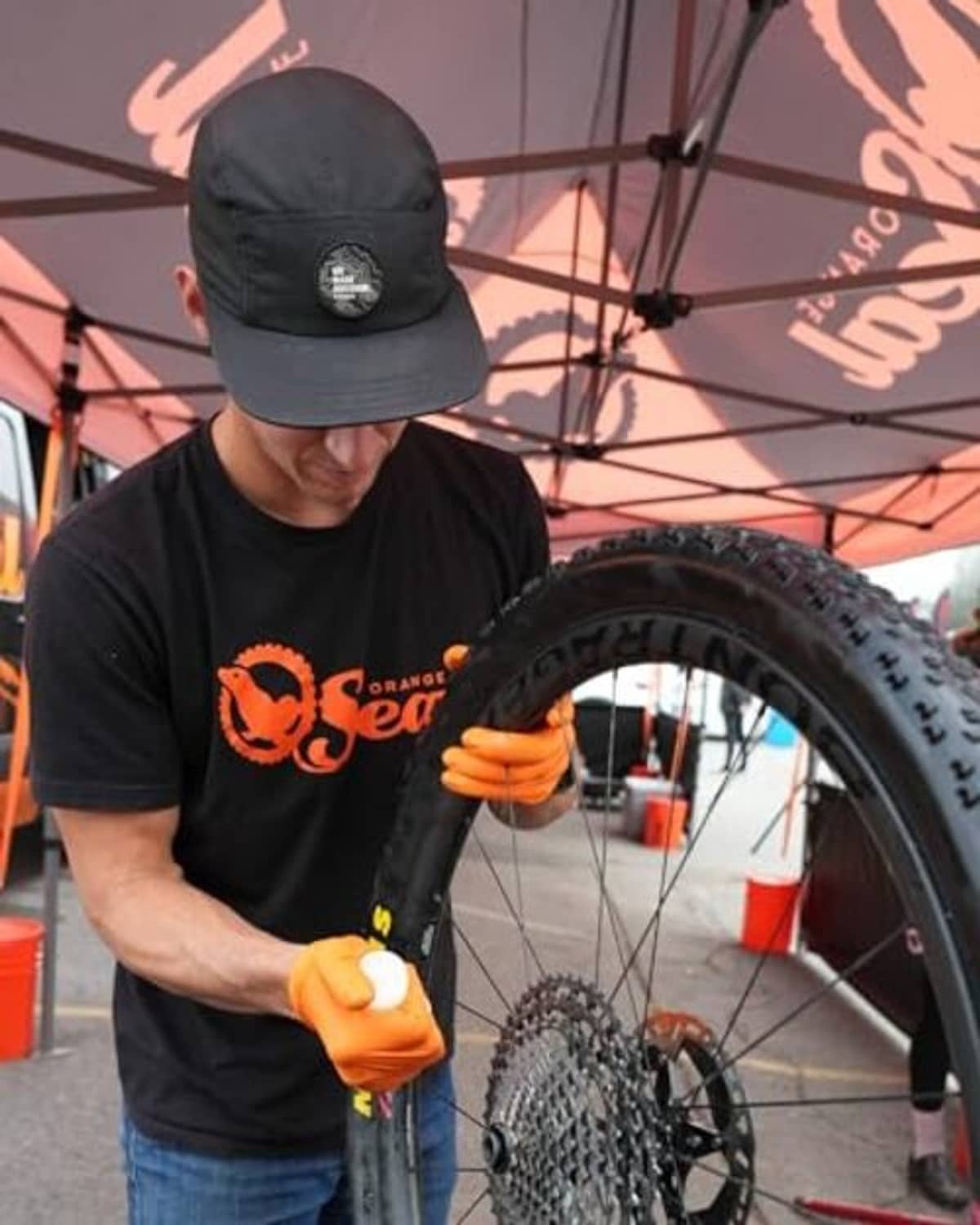 Orange bike tire sealant bottle in hand while repairing a bicycle tire at a shop
