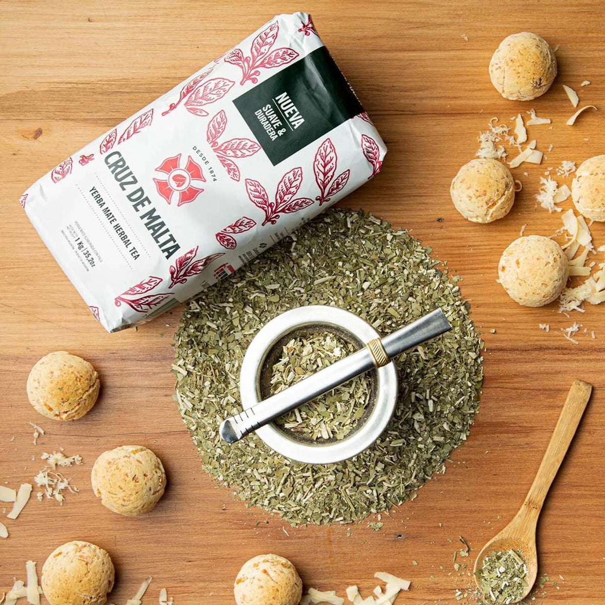 Yerba mate loose-leaf tea pouch with green leaves in a spoon and scattered leaf pieces