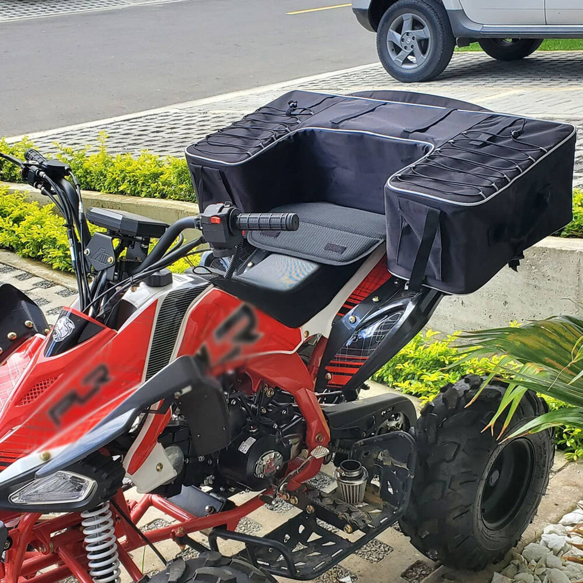 Black ATV rear seat storage bag mounted on a quad, with reflective stripe and straps