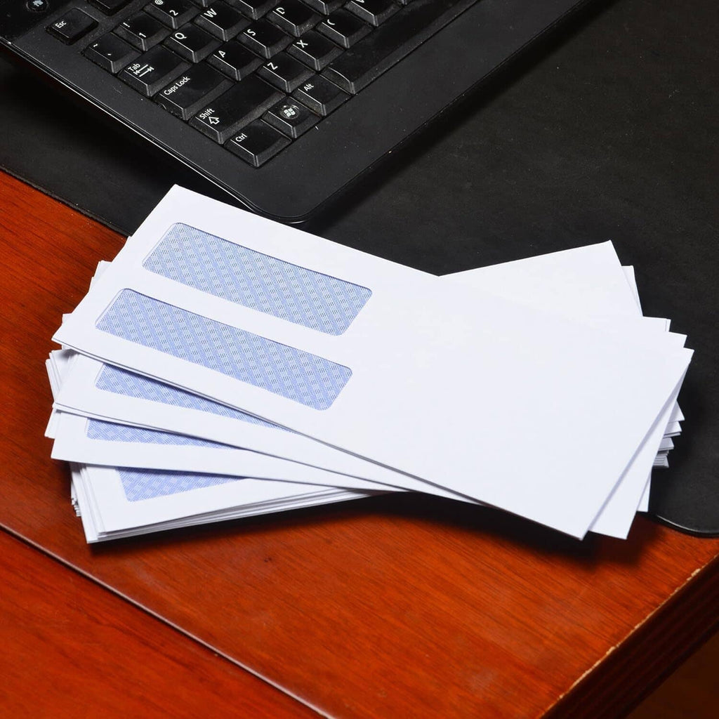 Stack of white security envelopes with double blue window strips on desk