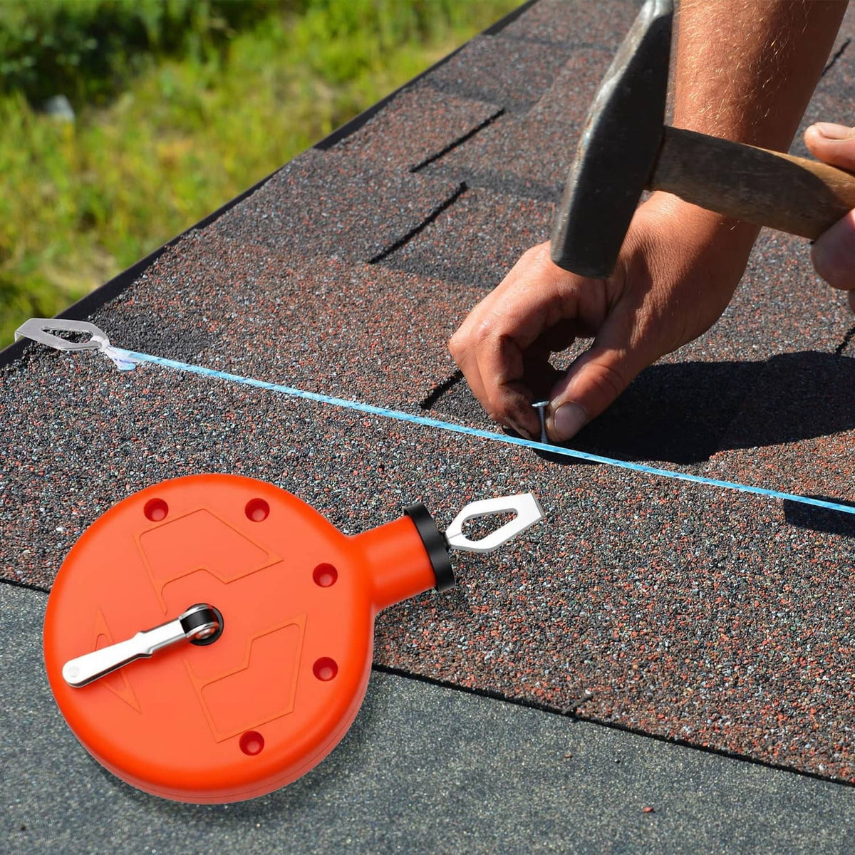 Orange chalk reel tool marking a straight blue line on asphalt