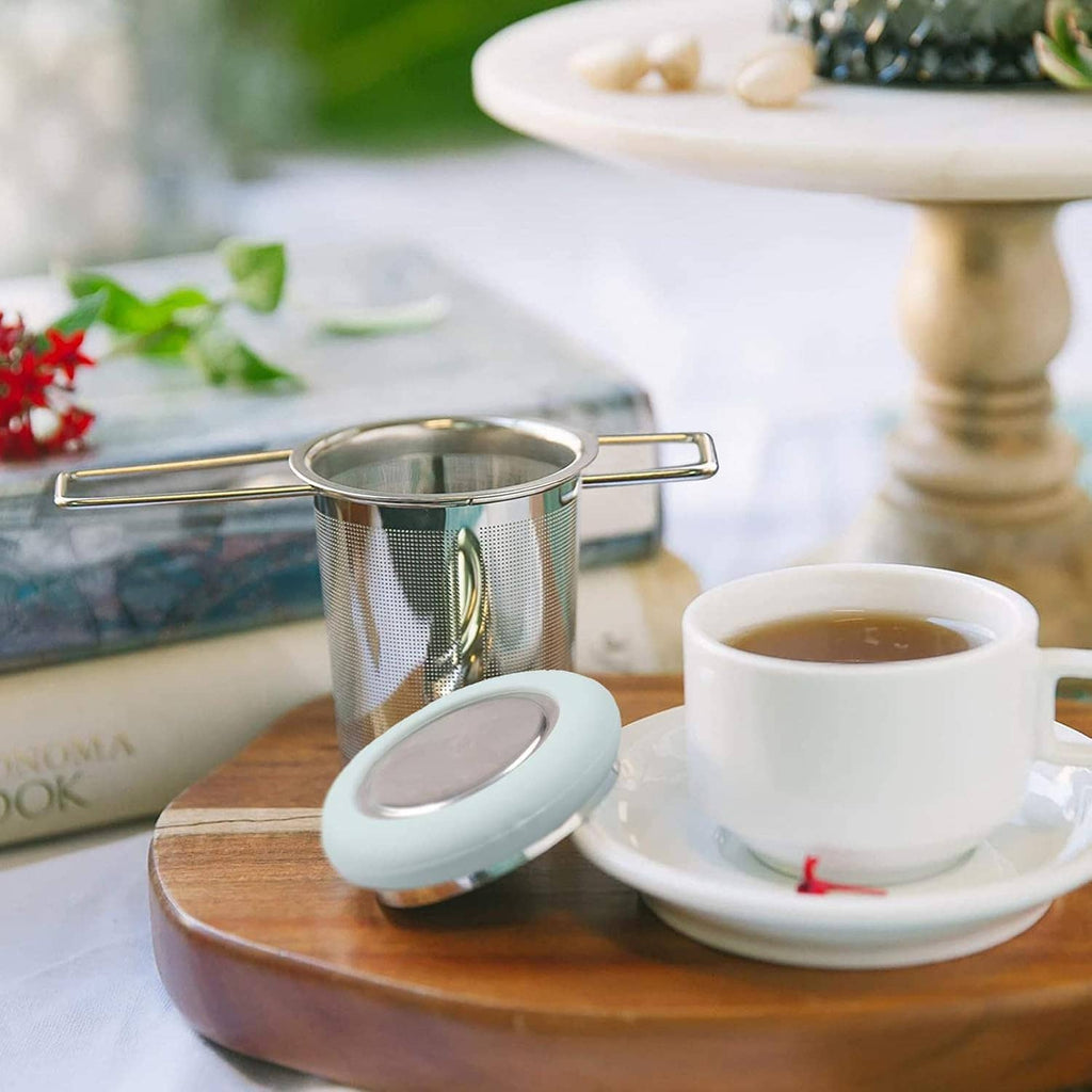 Stainless tea infuser with fine mesh basket and folding handle on a saucer