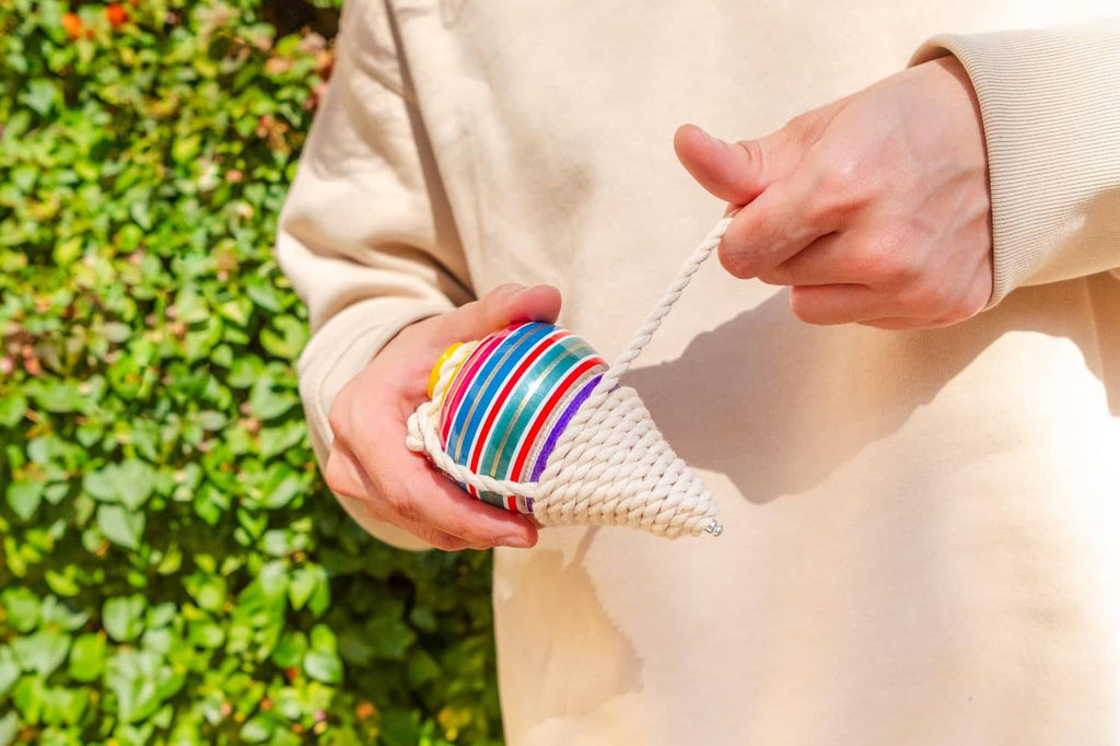 Multicolor striped wooden spinning top with white rope cord, held by hands