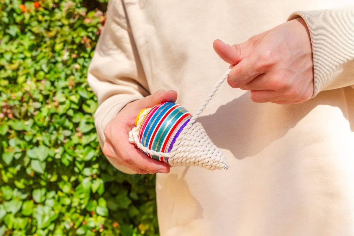 Multicolor striped wooden spinning top with white rope cord, held by hands