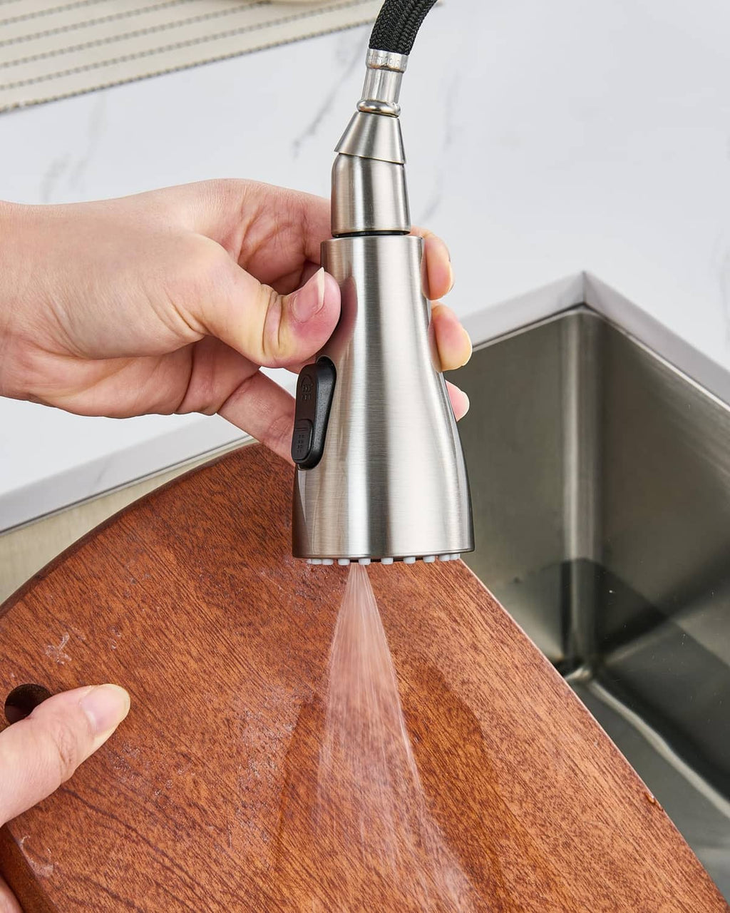 Hand holding brushed nickel faucet sprayer head over kitchen sink ledge