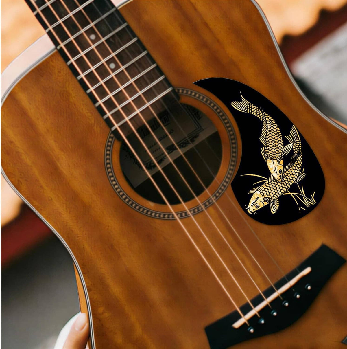 Close-up of acoustic guitar with black fish-pattern pickguard sticker and gold lines