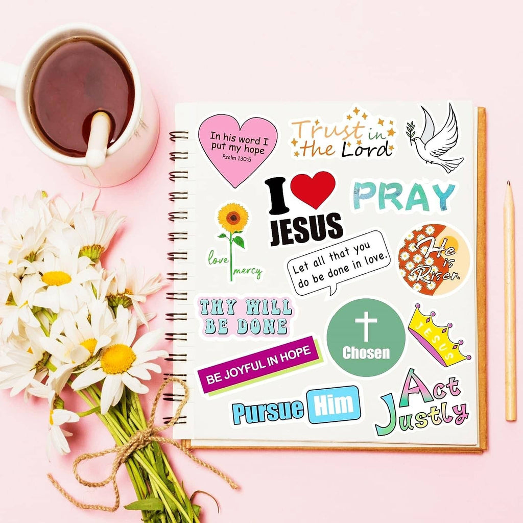 Christian quote stickers on a spiral notebook next to flowers and tea
