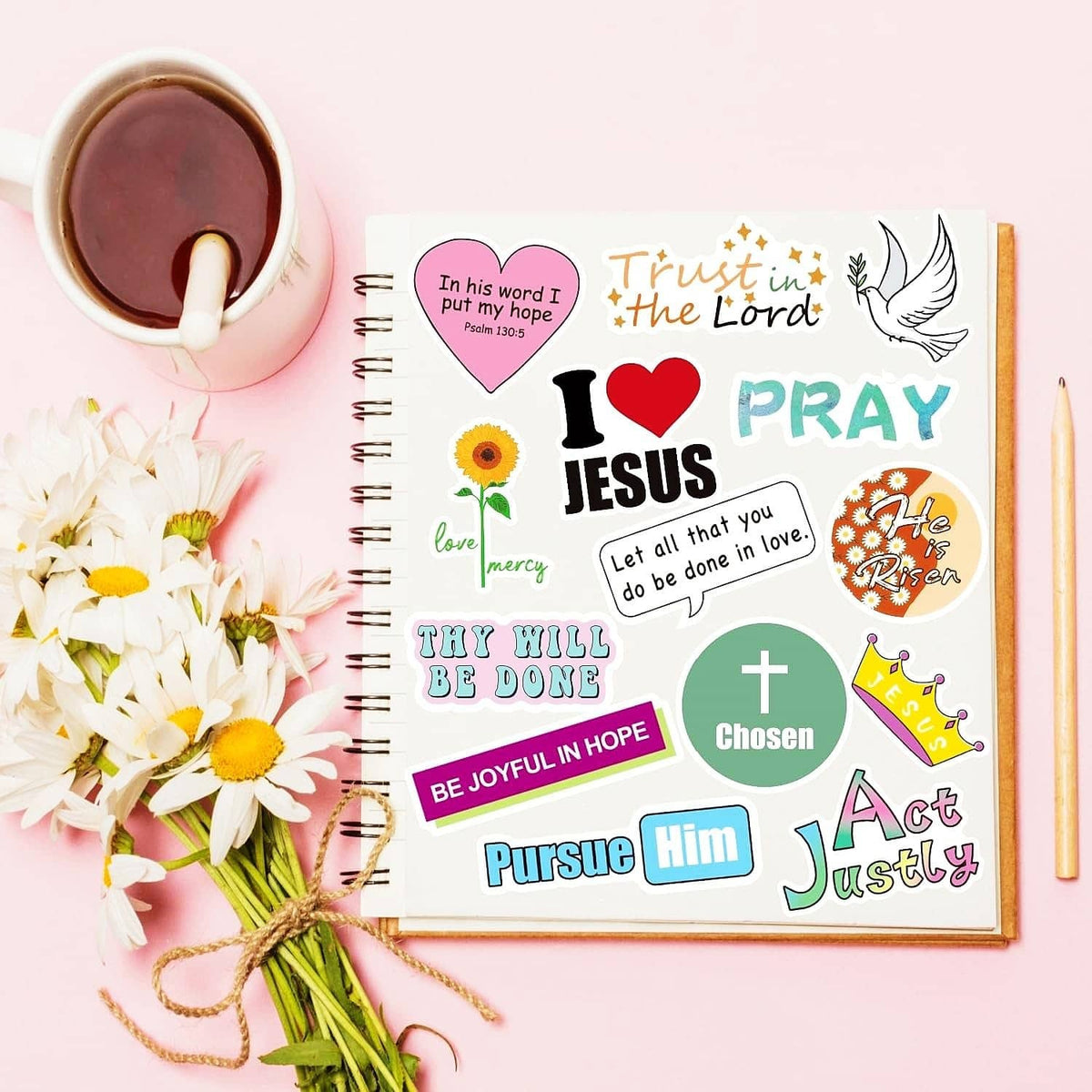 Christian quote stickers on a spiral notebook next to flowers and tea