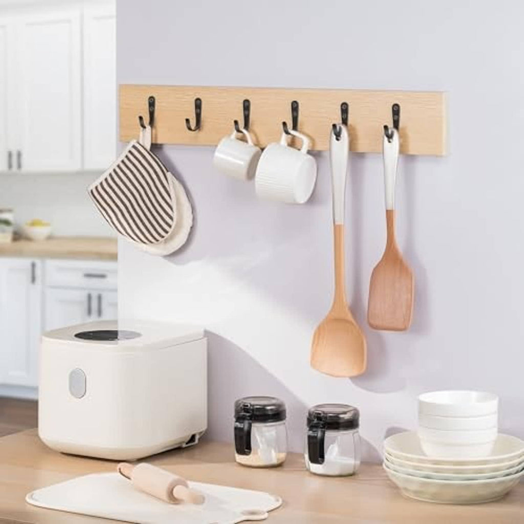 Black metal wall hooks holding kitchen utensils on a wooden rail