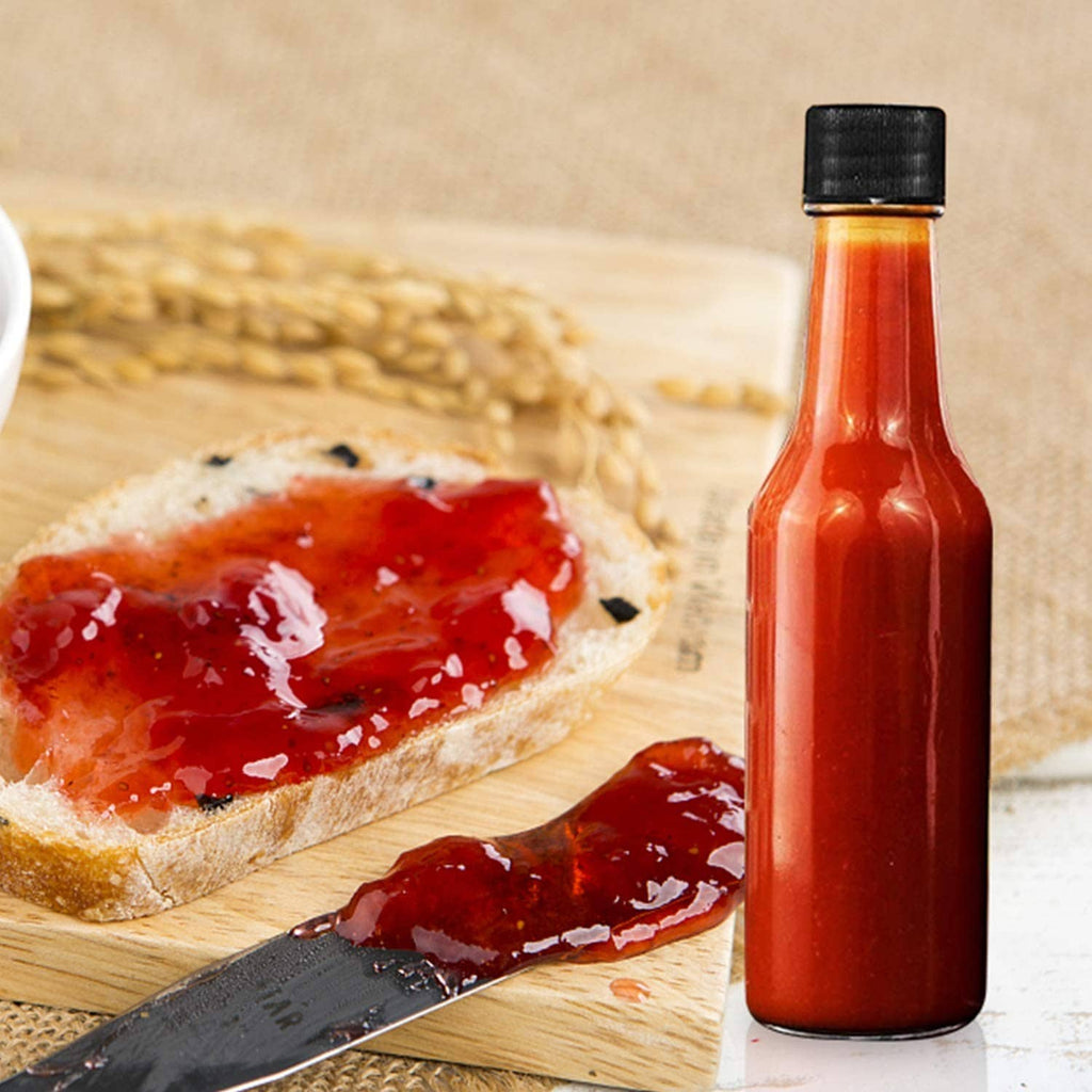 Glass hot sauce bottle with black cap beside toast with red spread on a board