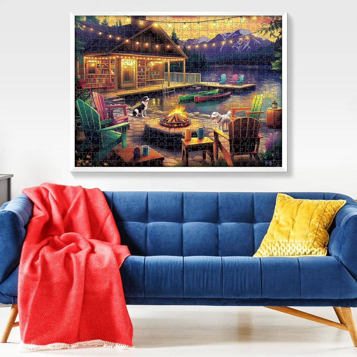 Framed lakeside bonfire jigsaw puzzle hanging above a blue sofa with red blanket