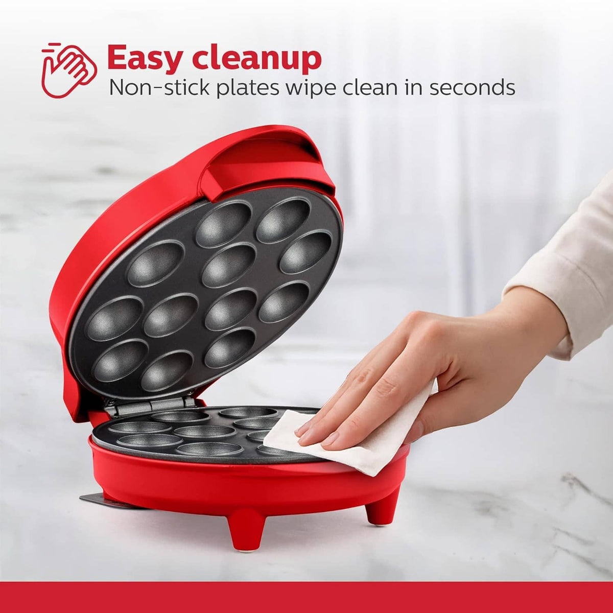 Red cake pop maker with non-stick plates open, being wiped clean with a cloth