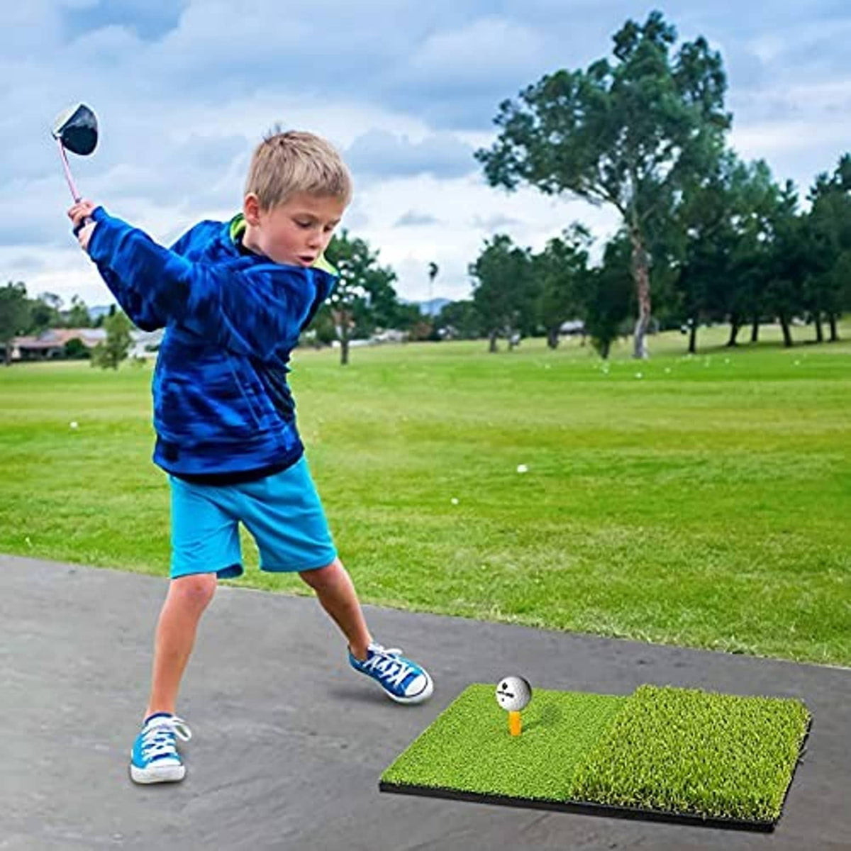 Green golf practice mat on pavement with a child swinging a club and ball