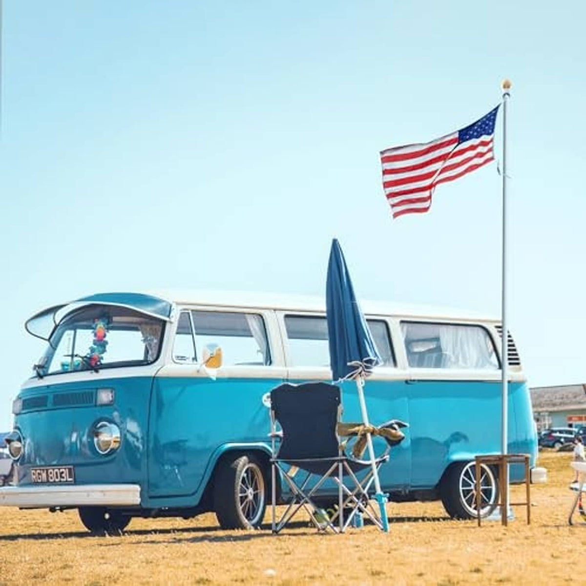Flag pole tire-mount base with flag on upright pole beside classic car